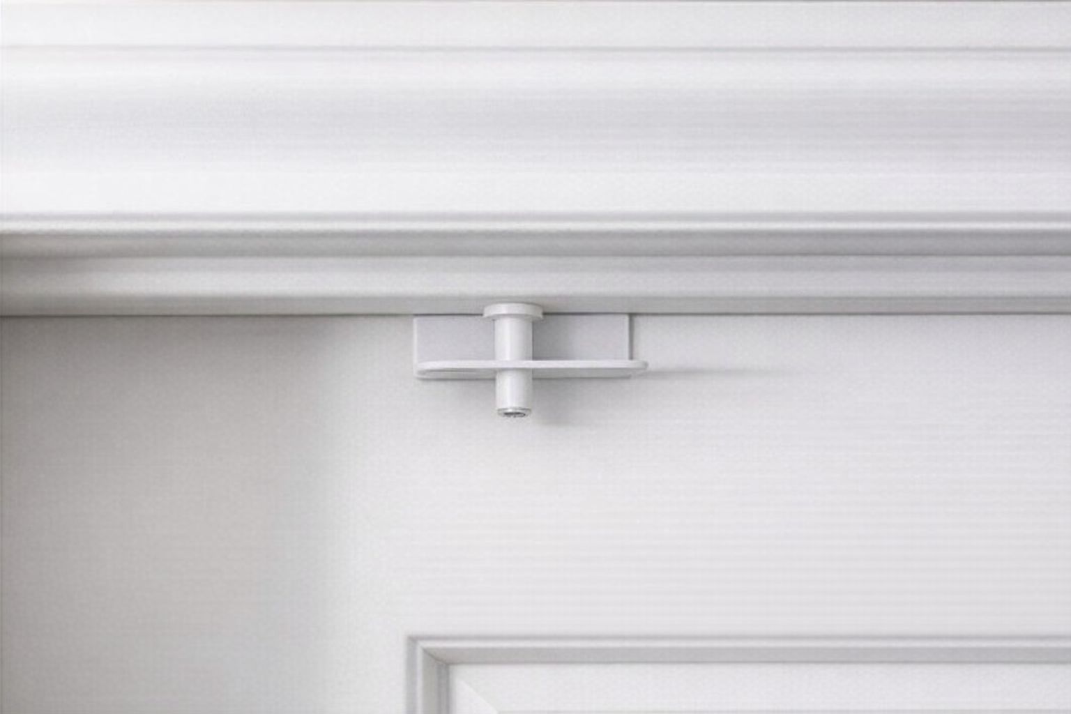 Närbild på en vit barnsäker dörrspärr monterad på en vit innerdörr.